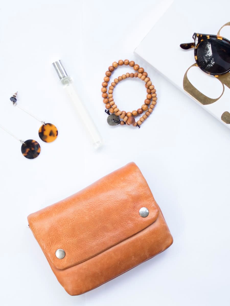 Flat lay of a tan leather wallet, sunglasses and a beaded bracelet