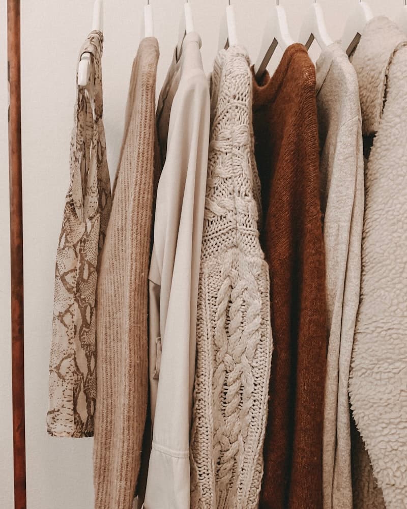 A rail of neutral-toned knitwear beside dried pampas grass