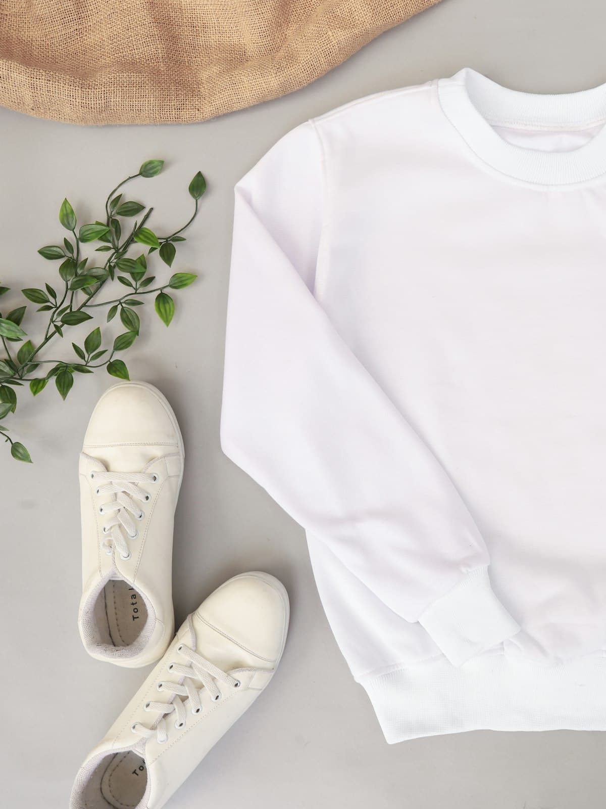 Flat lay of a white crewneck sweatshirt with jeans and white trainers