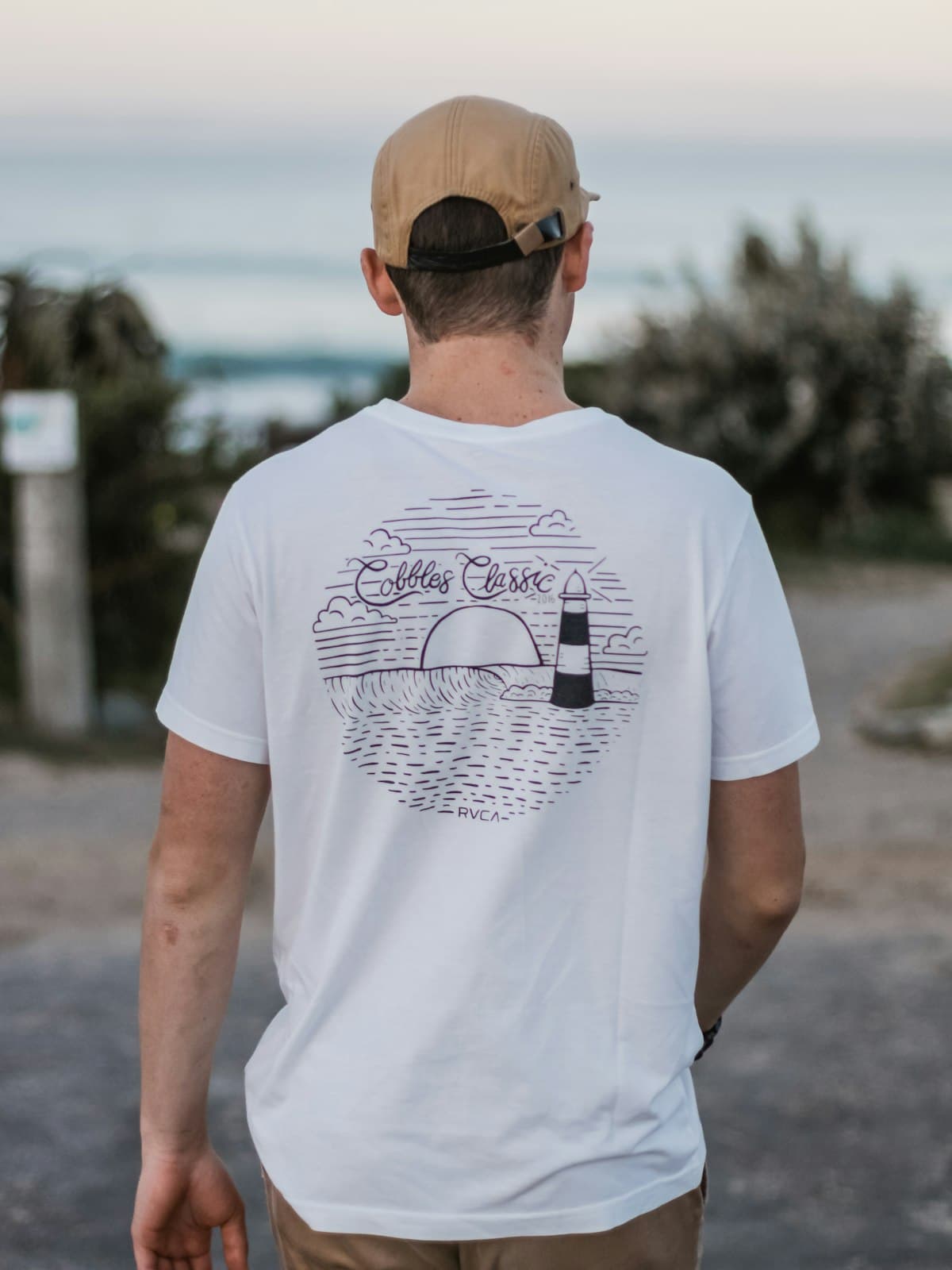 Model photographed from behind wearing a white tee with a coastal back print