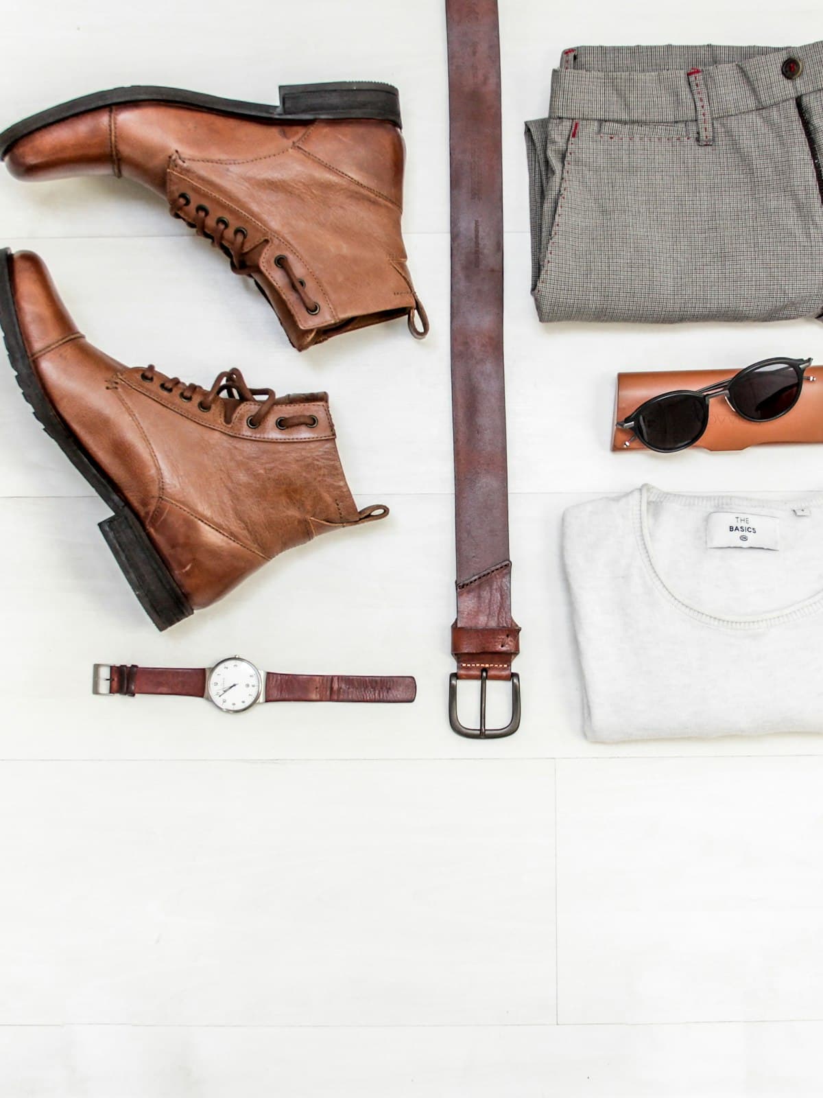 Flat lay of brown leather boots, grey trousers, a leather belt and a white tee