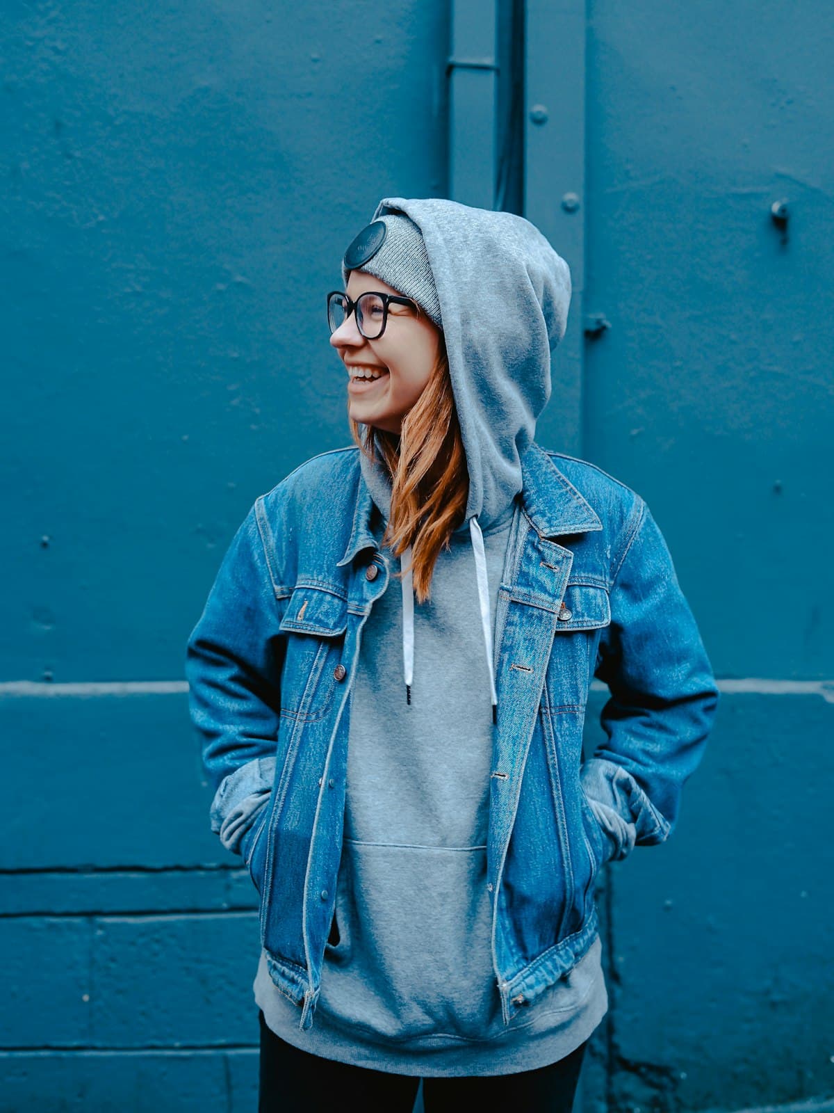 Model wearing an indigo denim jacket over a grey hoodie against a teal wall