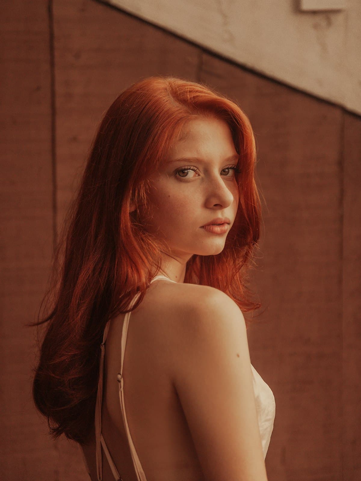 Model wearing an ivory satin slip dress against a warm terracotta wall