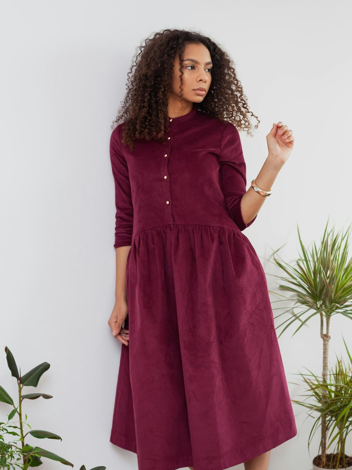 Model wearing the Margot burgundy corduroy shirt dress beside houseplants