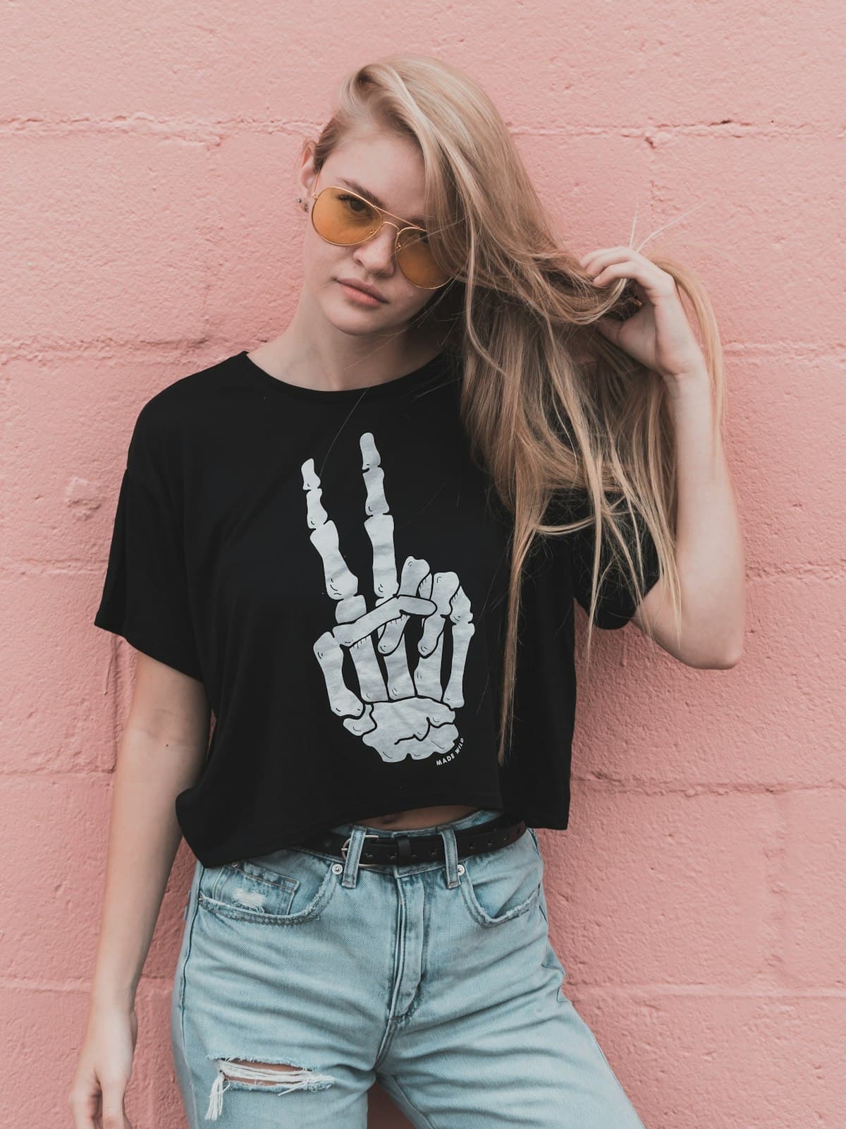 Model wearing the Noir black graphic crop tee with ripped jeans against a pink wall