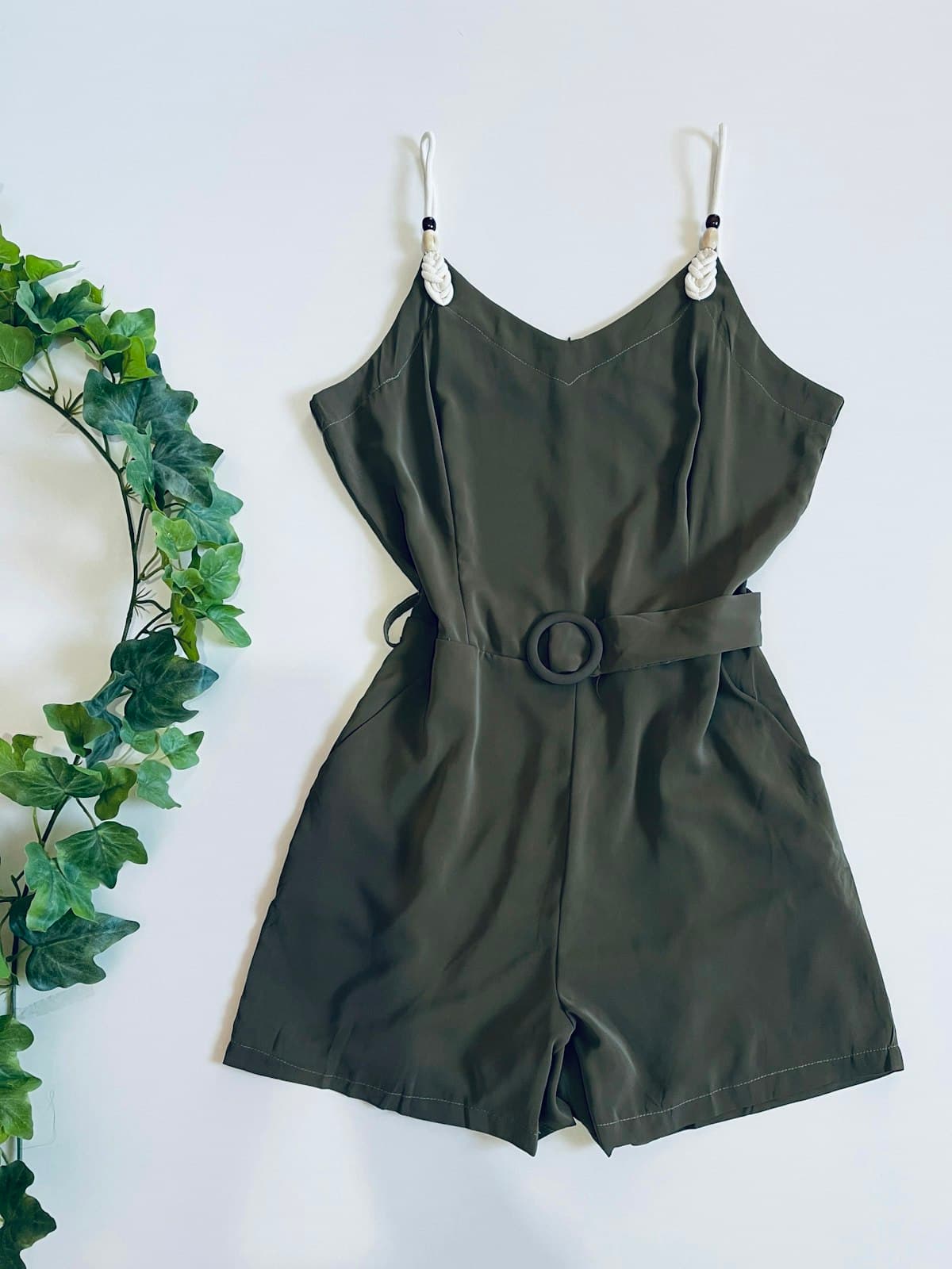 Olive green belted playsuit laid flat beside trailing ivy
