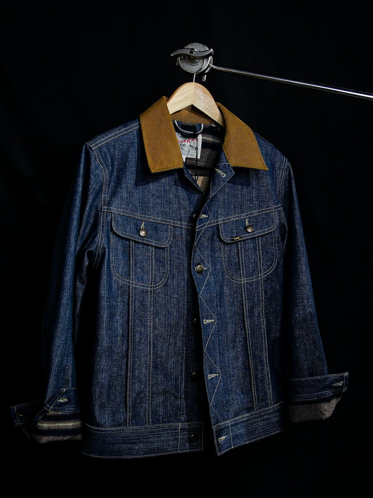 Indigo selvedge denim jacket with a tan corduroy collar shown on a hanger