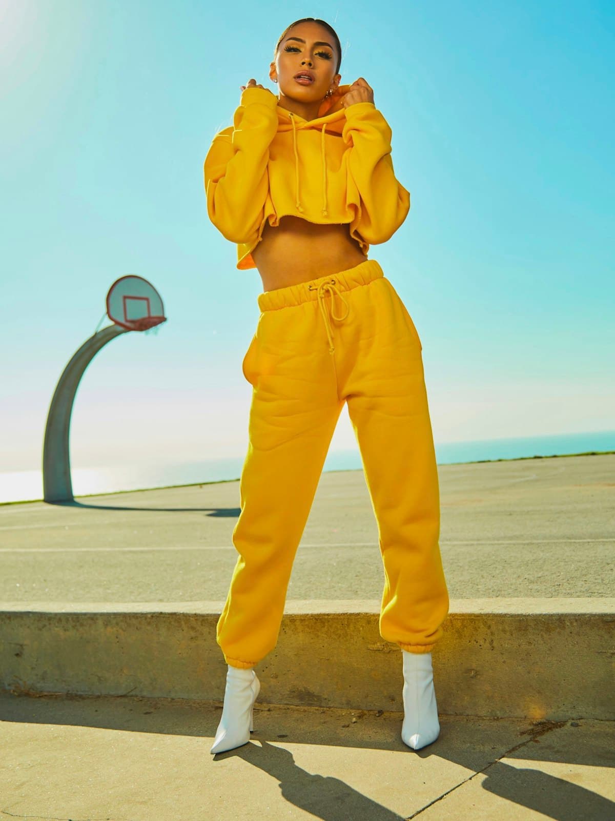 Model wearing a yellow cropped hoodie and matching joggers on an outdoor court