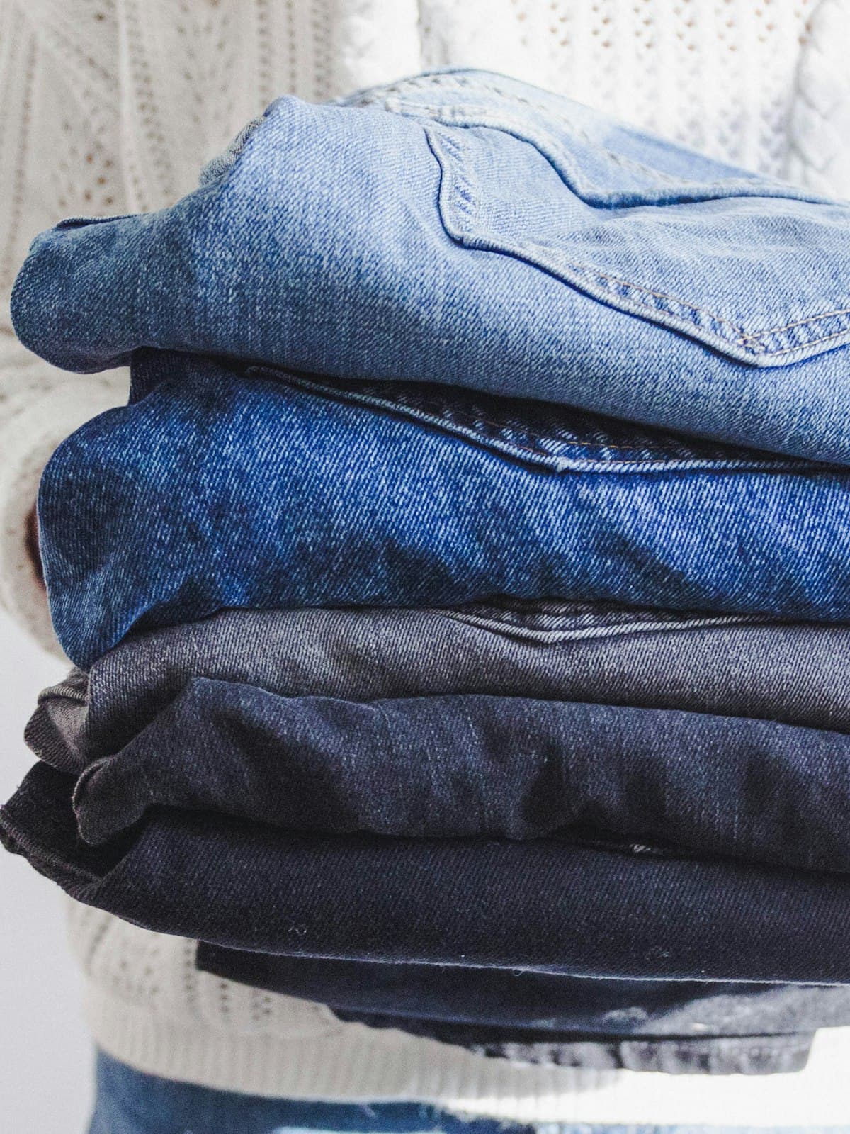Stack of folded denim in several washes held in someone's arms