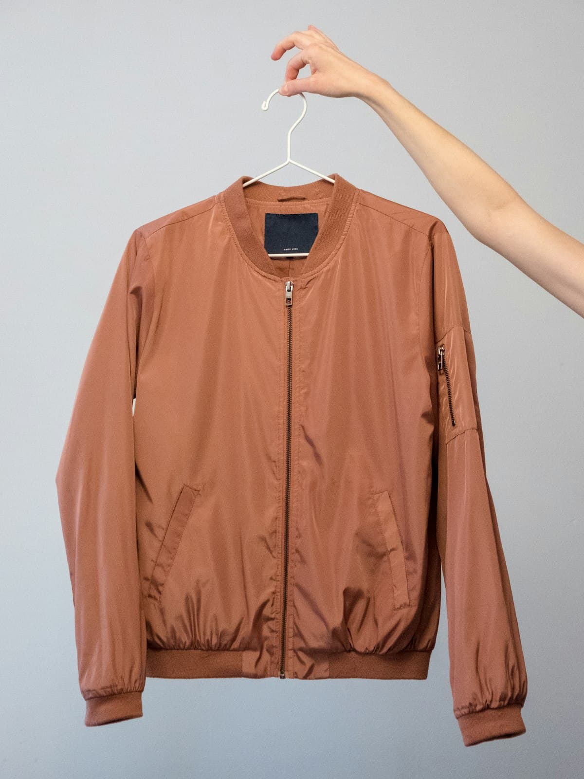 Terracotta lightweight bomber jacket shown on a hanger against a grey wall