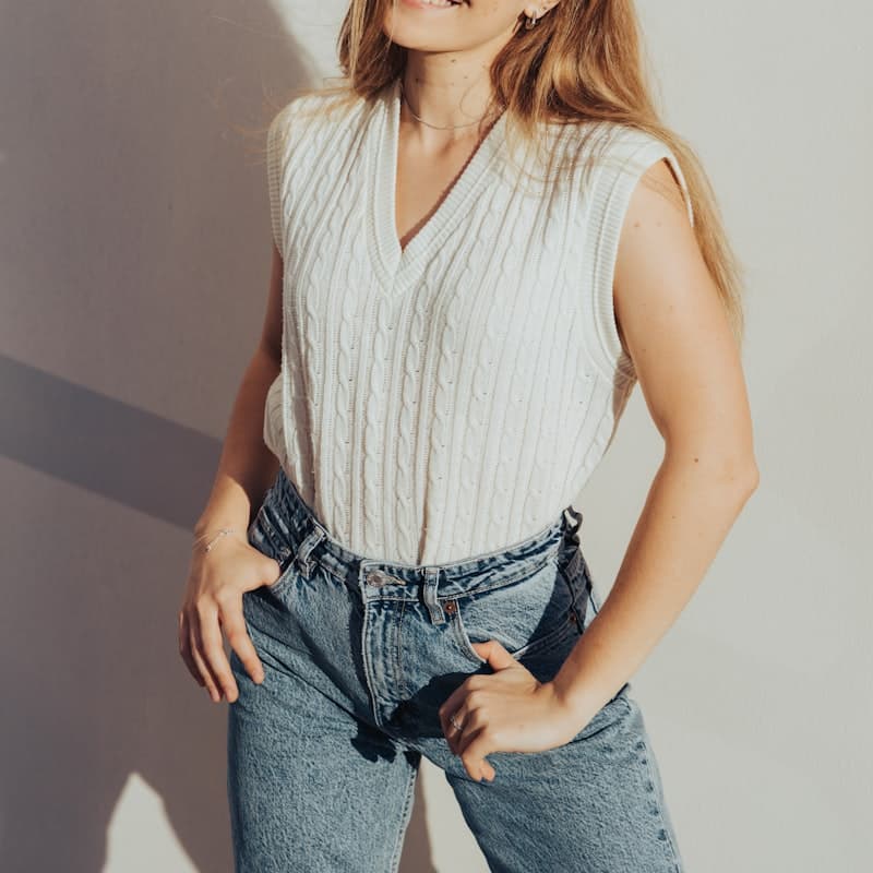 Model in a cream cable-knit vest with light-wash denim